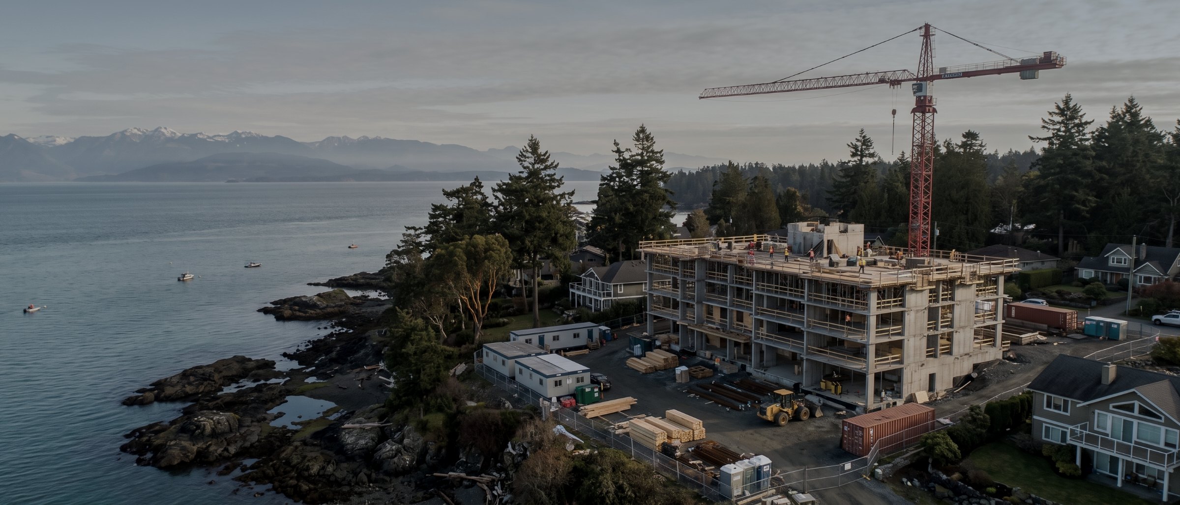 Aerial view of a mid-rise construction site with a tower crane beside the ocean on Vancouver Island