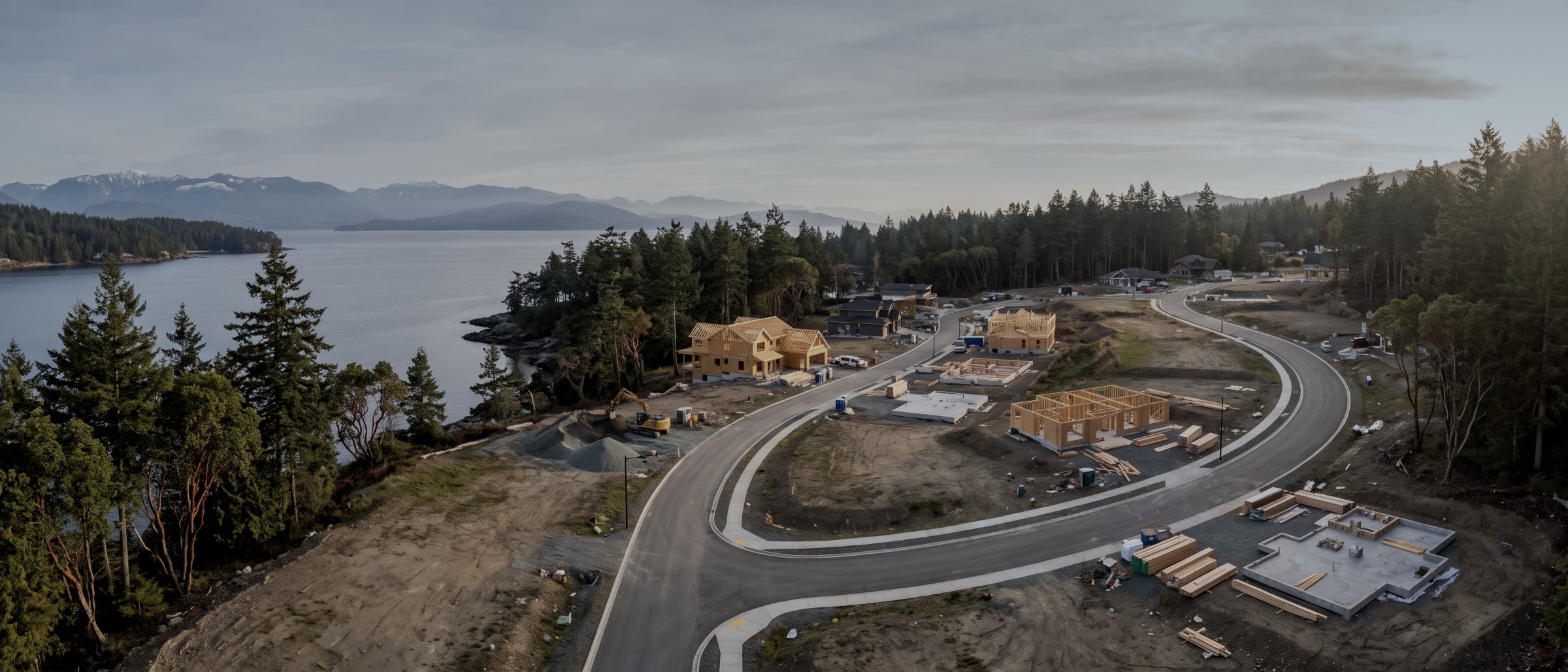 Aerial view of a new residential development with curving roads, graded lots and timber framing beside the water
