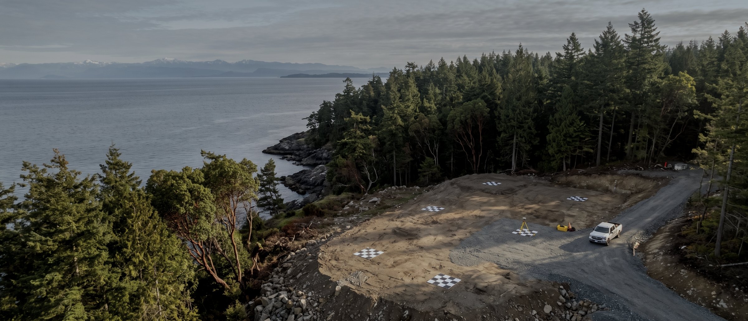 Aerial view of a graded survey site with ground control targets laid out, forest and ocean beyond