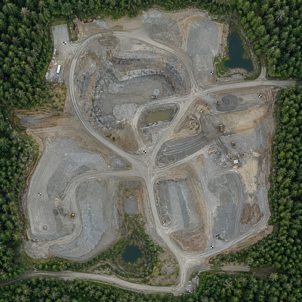 Orthomosaic of a quarry, north up, with haul roads, benches, settling ponds, plant buildings and equipment legible, and black-and-white ground control targets distributed across the site